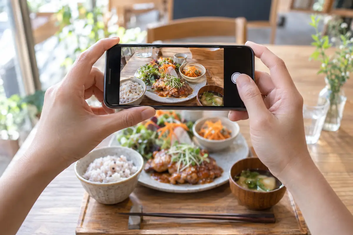 明るい店内でスマートフォンを構え、料理の写真を撮っている店主の手元